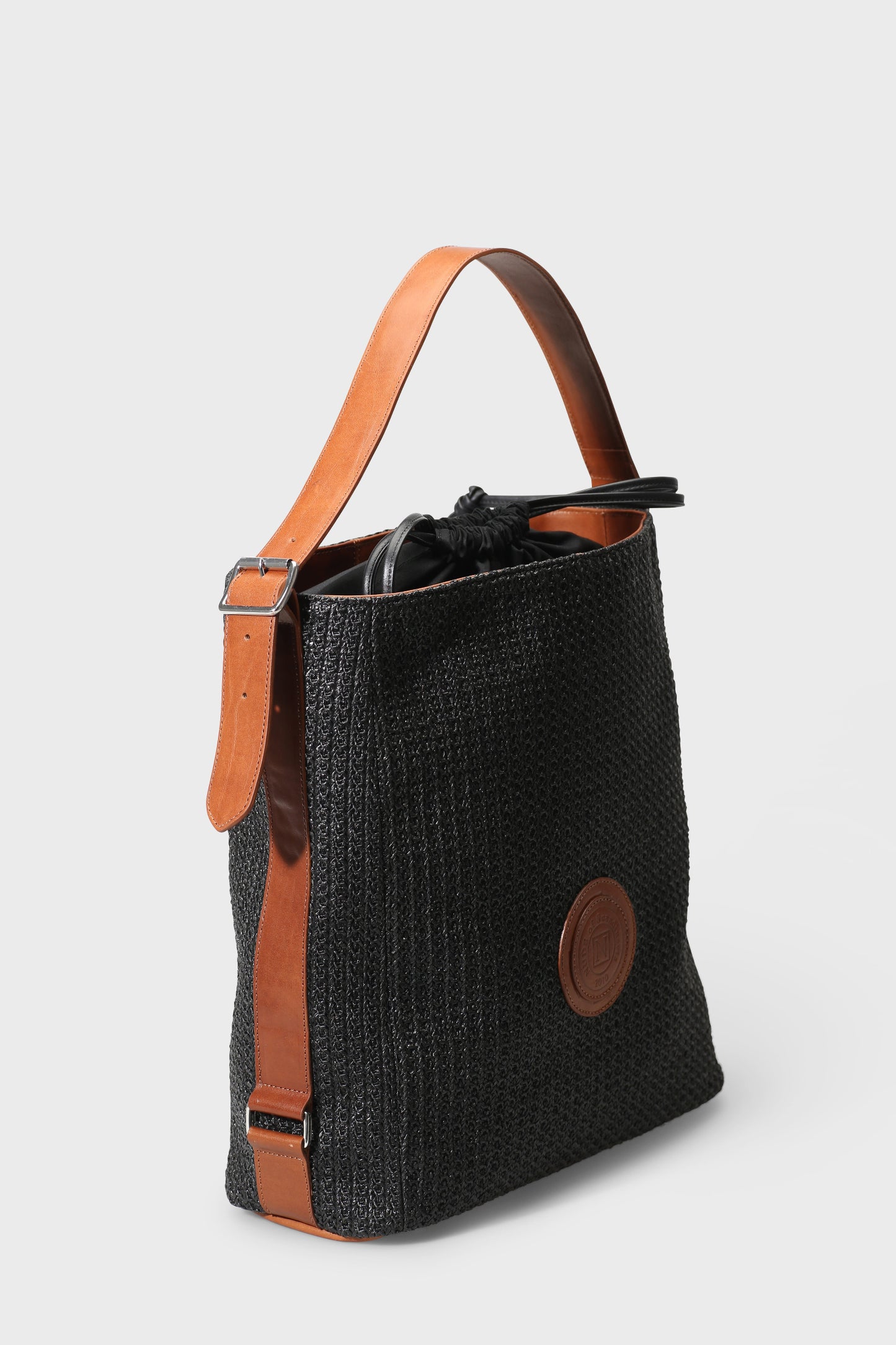 Black textured bag with brown leather accents on a light gray background