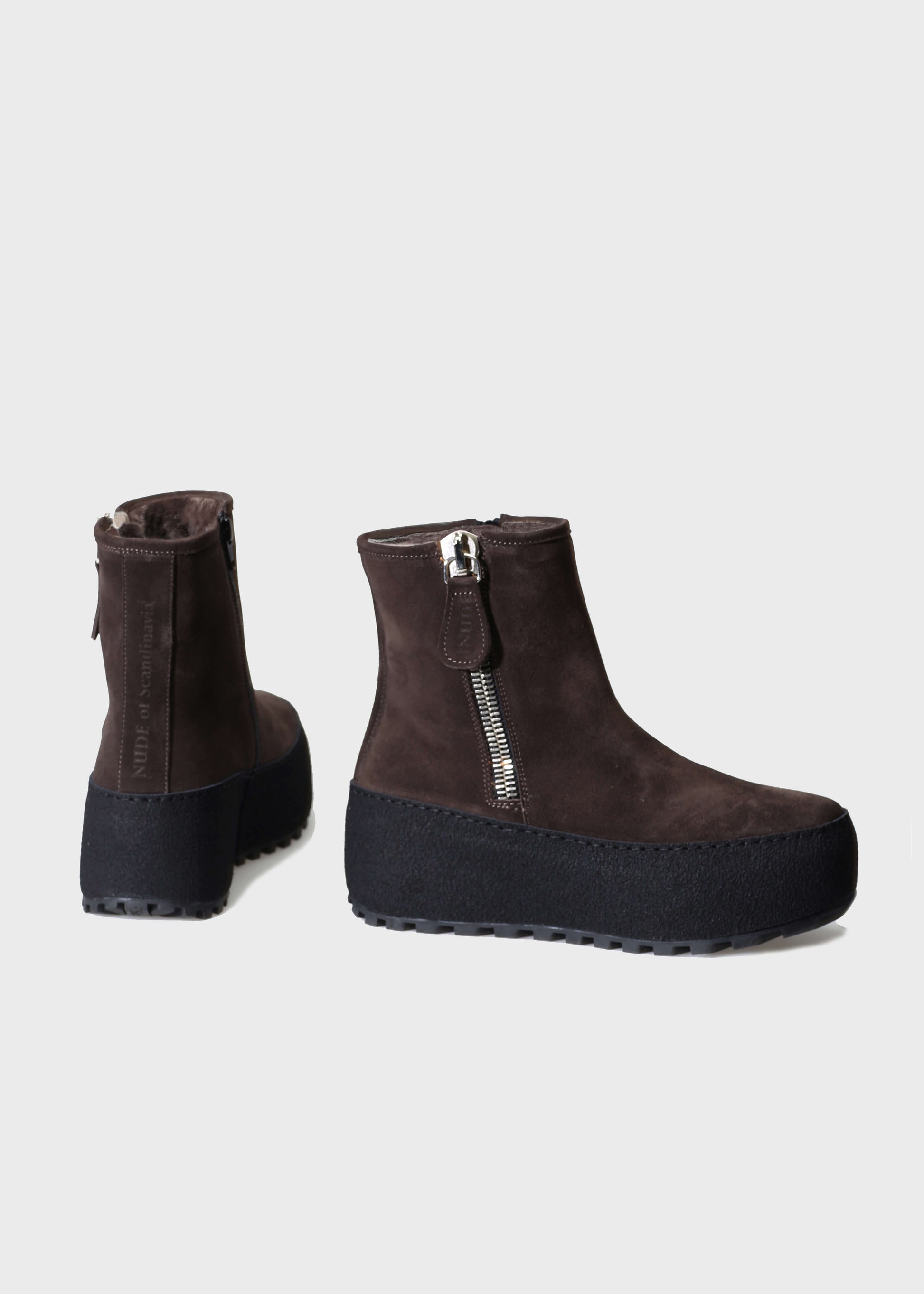 Brown suede ankle boots with zippers on a light gray background